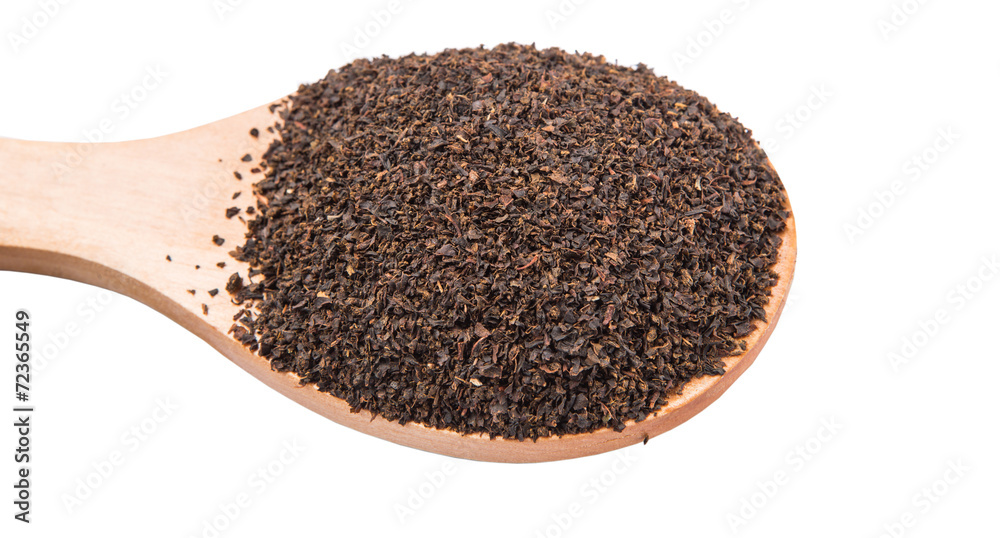 Dried, processed tea leaves in wooden spoon over white Dried, processed tea leaves in wooden spoon over white