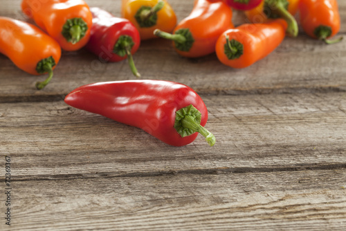 Fotografia Red sweet pepper with other peppers on rough wood surface