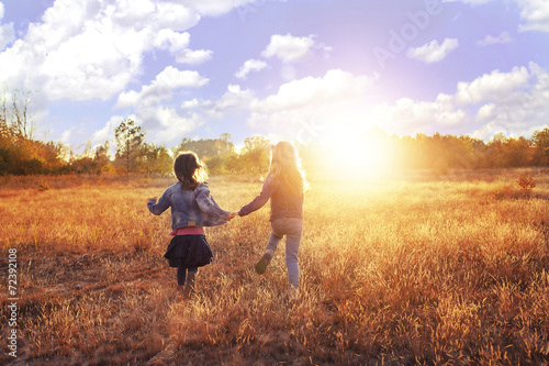 Two young girls runs on the sunny meadow