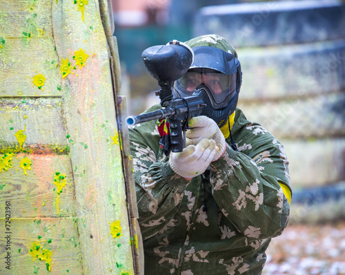 Man in camouflage with paintball gun behind fortification