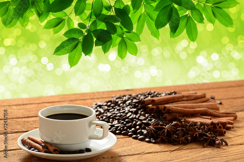 a cup of coffee on wooden table with green leaves background