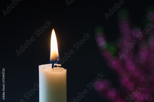 One burning candle at blurred heather