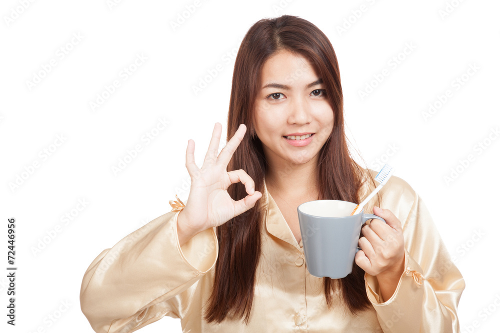 Asian woman in pajamas show OK with toothbrush in mug Asian woman in pajamas show OK with toothbrush in mug