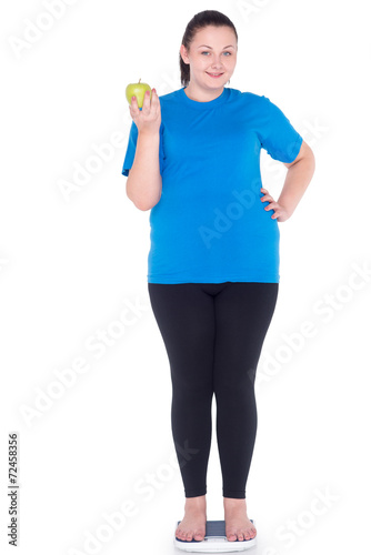 Smiling overweight woman with apple on weighs