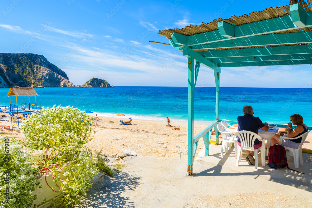 Tourists Sit In Greek Tavern On Petani Beach Kefalonia Island Stock tourists-sit-in-greek-tavern-on-petani-beach-kefalonia-island-stock