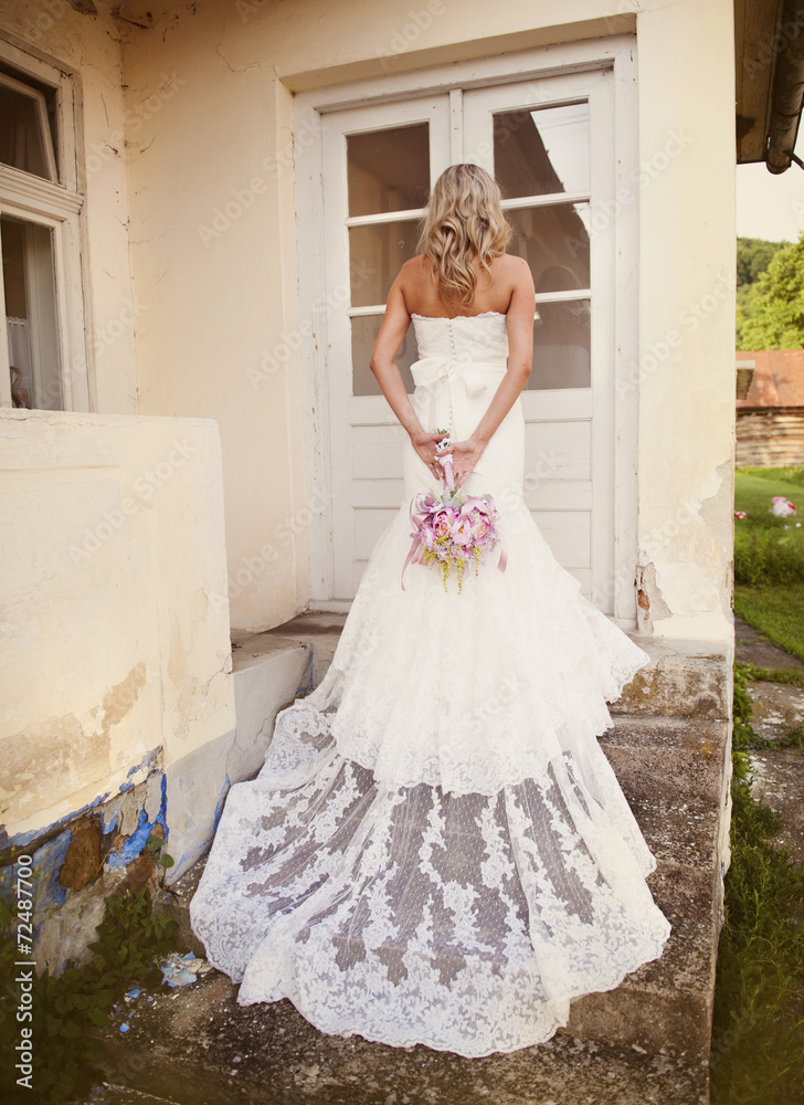 Fototapeta premium Blonde bride with veil by old house