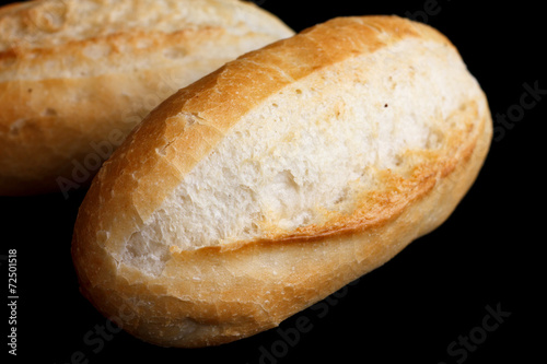 Whole white mini baguettes on black background.