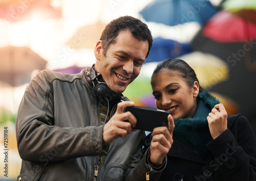 Cheerful man and woman friends looking at mobile smart phone