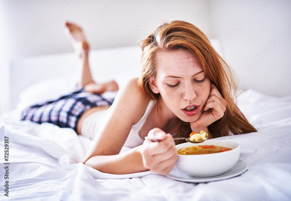 recovering woman in bed eating chicken soup while sick