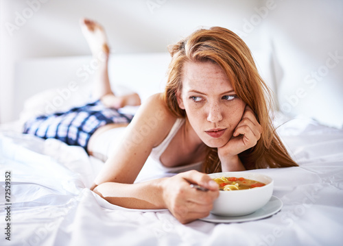 woman in bed eating chicken noodle soup while sick