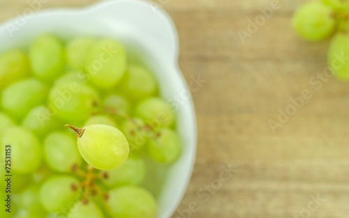 Selective focus of a single grape over a bowl of grapes