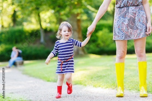 mother and little adorable child girl in rubber boots having fun