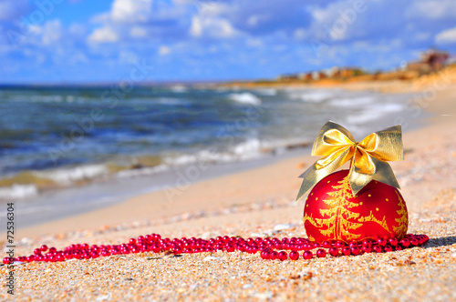 Red christmas ball with golden bow on the sand