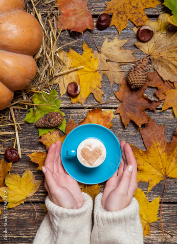 Female holding cup of coffee on autumn background.