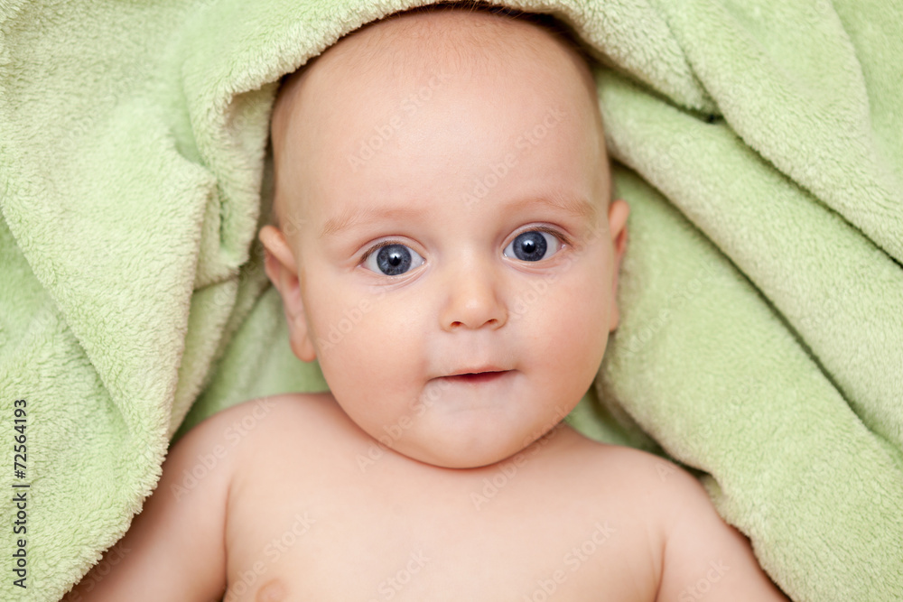 Caucasian baby boy covered with green towel joyfully smiles at c Caucasian baby boy covered with green towel joyfully smiles at c