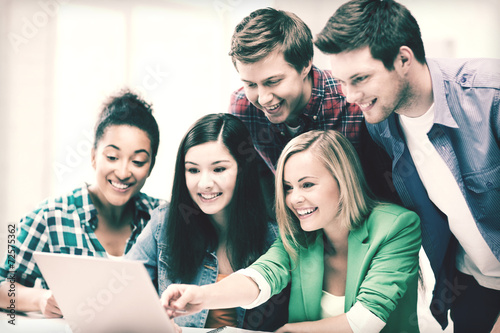 smiling students looking at laptop at school