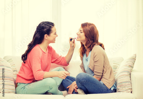 two smiling teenage girls applying make up at home