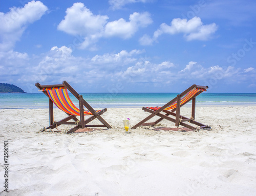 Two beach chairs on the white sand beach before blue sea