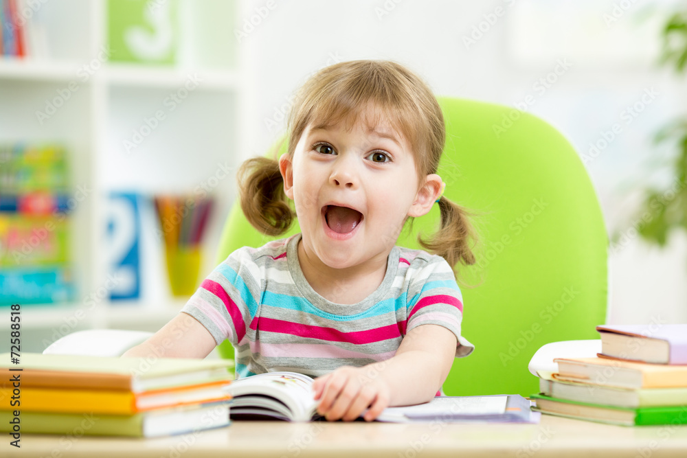 Happy kid reading book at table in nursery Happy kid reading book at table in nursery