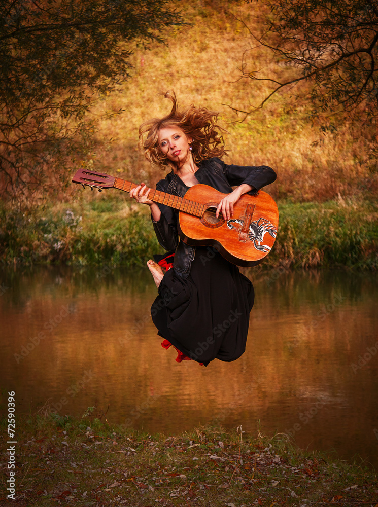 Fototapeta premium Young woman jumping with guitar