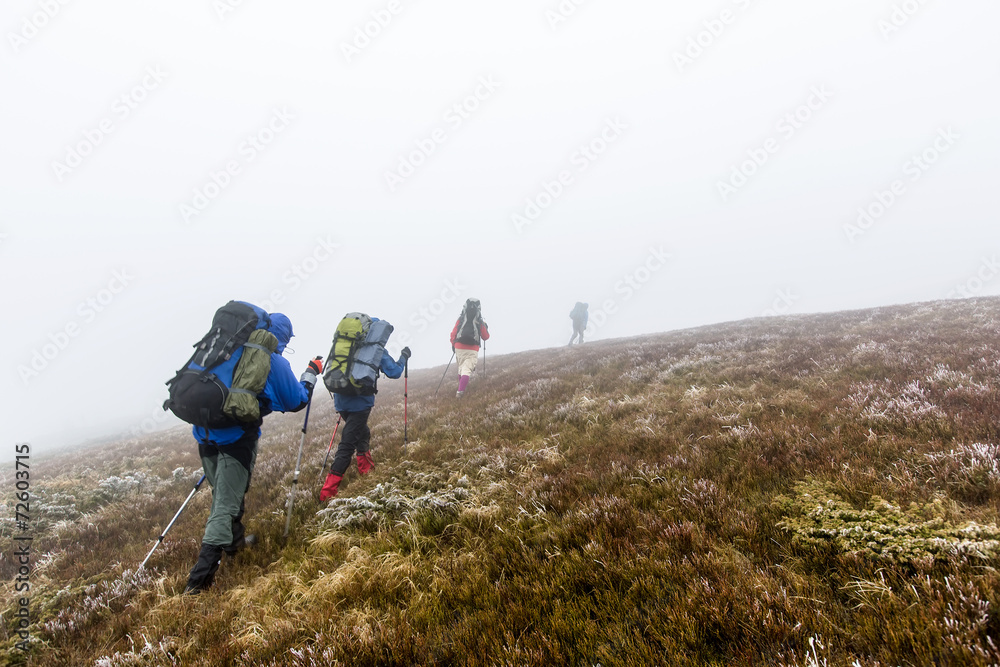 Group of hiker are walking in mountains covered with dense cloud