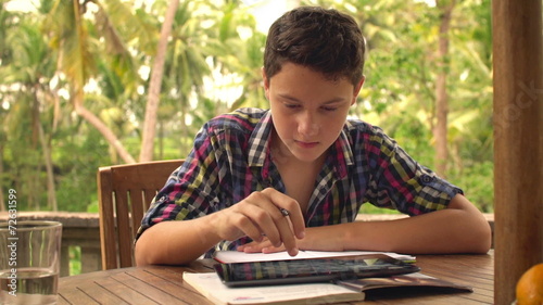 Young teenager doing homework and using tablet computer on terra