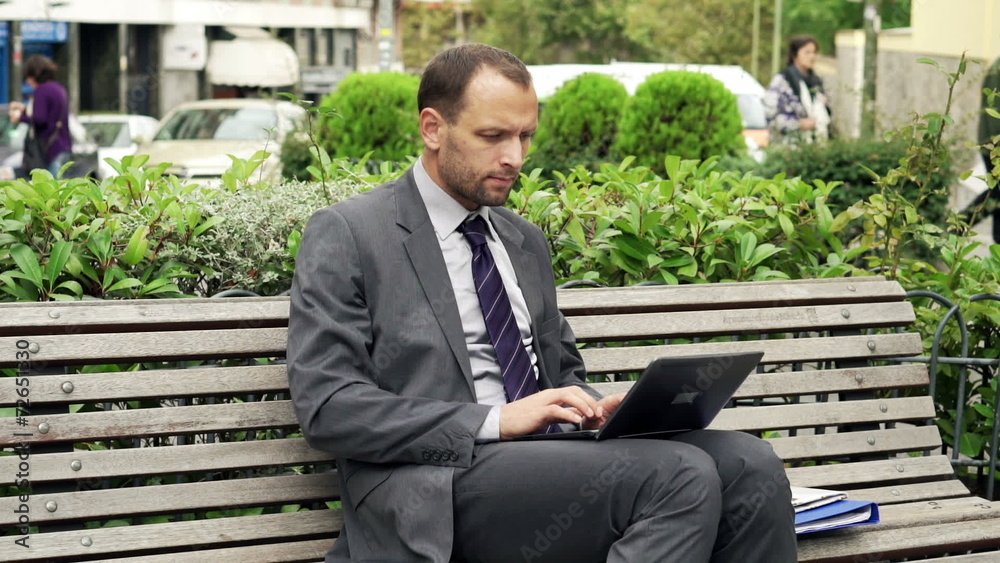 Young businessman working on laptop sitting on the street bench Young businessman working on laptop sitting on the street bench