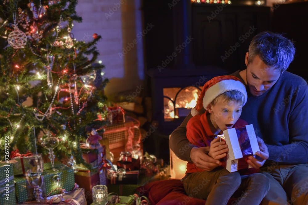 Lovely little boy with a santa claus hat and his father opening