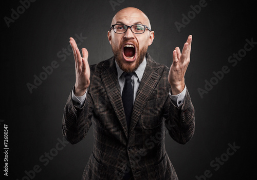 Man with glasses, a beard, shouting. Widely puts hands.