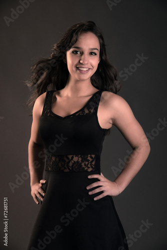 Smiling cute brunette teenage girl wearing black dress. Studio f