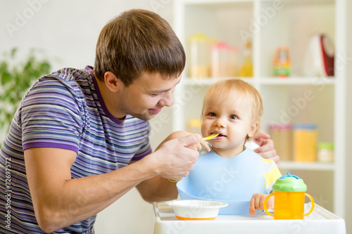 young father teaches his baby son to eat with spoon