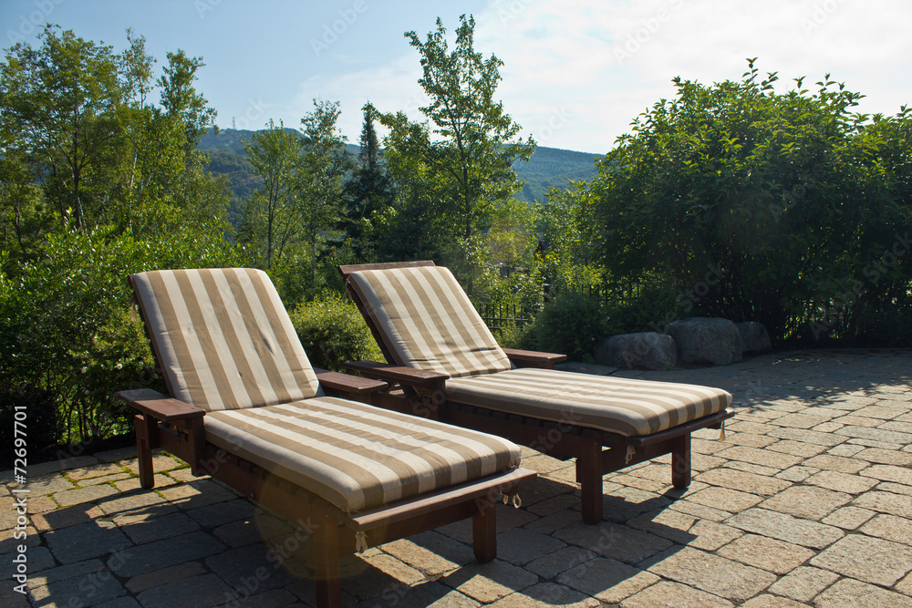 A pair of sunbathing lawn chairs outside on a deck