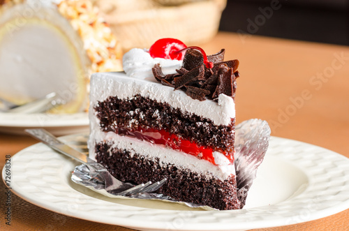 Piece of cake chocolate and cherry topping on white dish