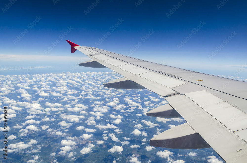 Wing of airplane flying above the clouds in the sky Wing of airplane flying above the clouds in the sky