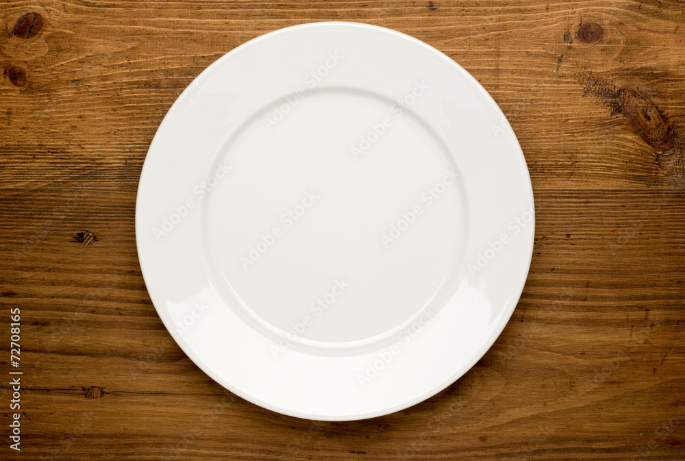 Empty white plate on wooden table Empty white plate on wooden table