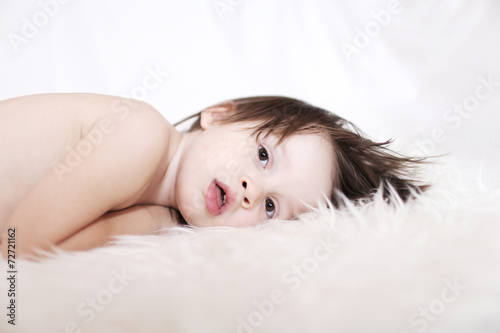portrait of 2 years lovely child lying on white fur rug