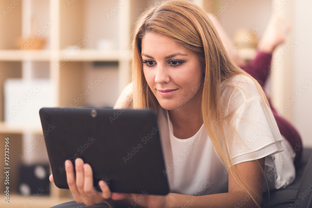Smiling young woman looking on your tablet sitting on sofa at ho Smiling young woman looking on your tablet sitting on sofa at ho