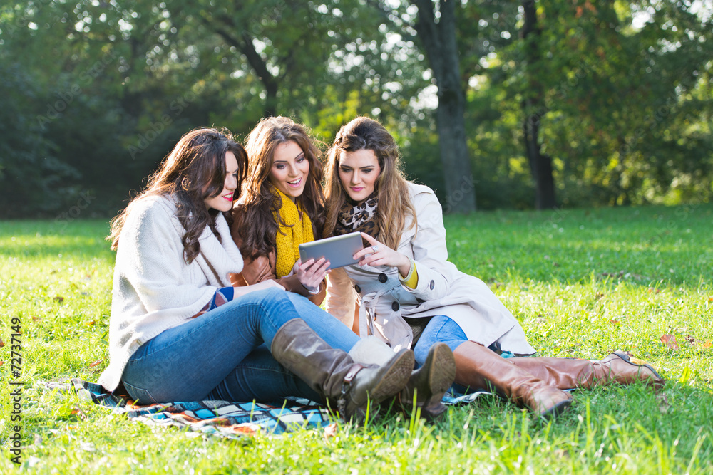 Three beautiful women using a tablet in the park Three beautiful women using a tablet in the park