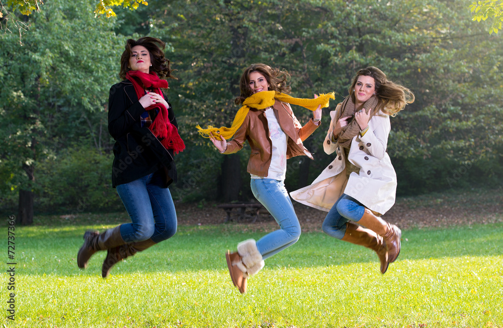 Fototapeta premium Three young women jumping joyfully in the park
