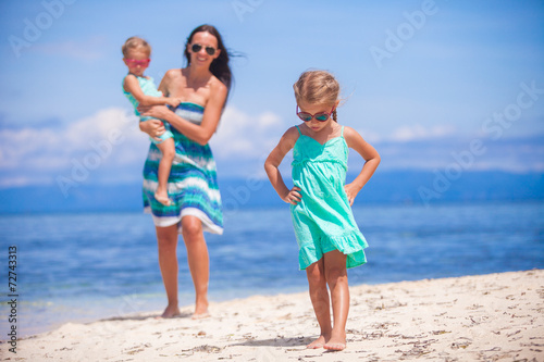 Adorable little girls and young mother on tropical white beach