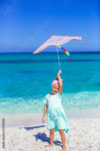 Little happy girl playing with flying kite on tropical beach
