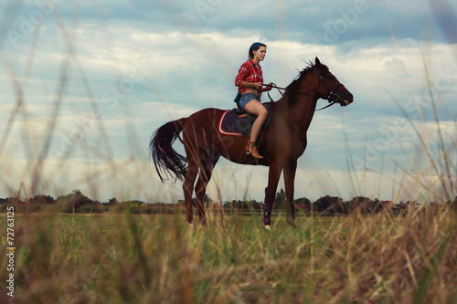 Young woman with red plaid shirt riding horse outdoor