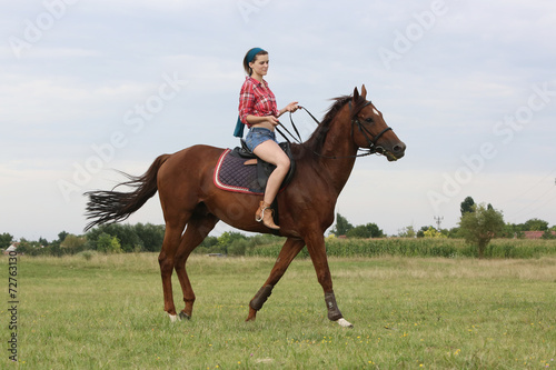Young woman with red plaid shirt riding horse outdoor