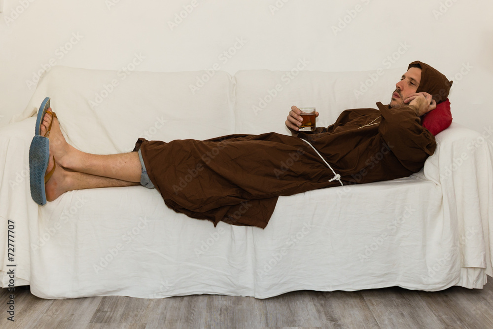 Fototapeta friar drinking and relaxing lying on a white sofa