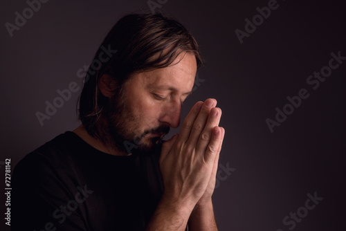 Adult bearded man praying in dark room