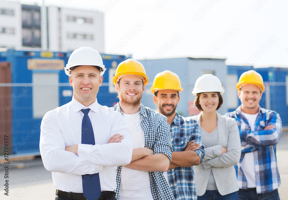 group of smiling builders in hardhats outdoors group of smiling builders in hardhats outdoors