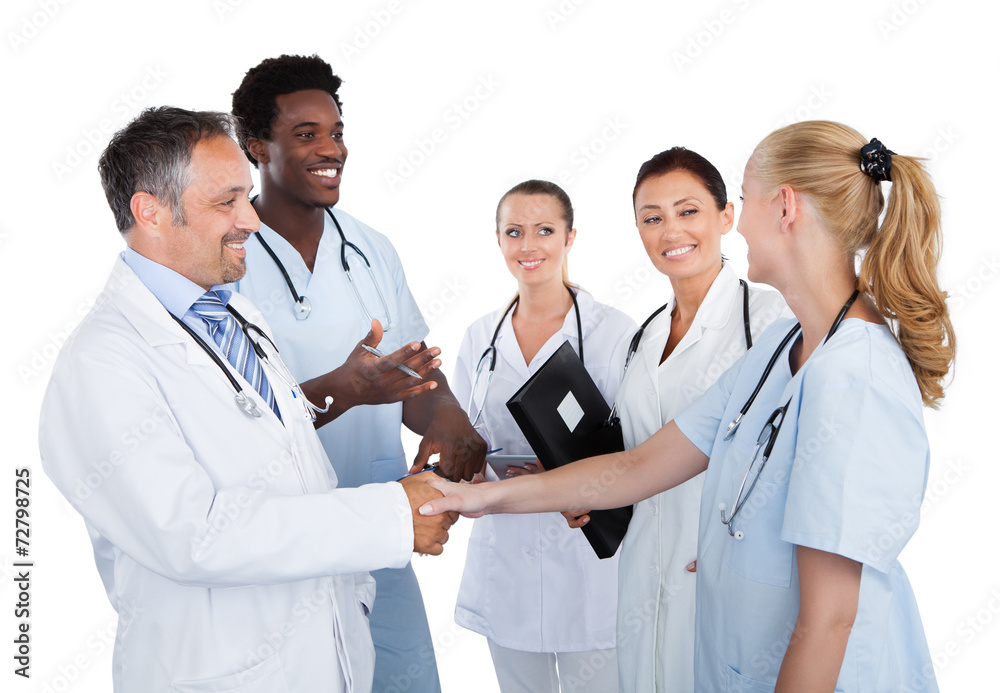 Doctors Making Handshake While Colleagues Looking At Them Doctors Making Handshake While Colleagues Looking At Them