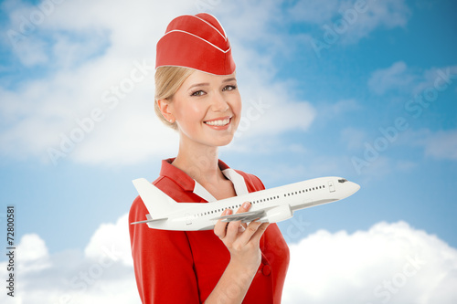 Charming Stewardess Holding Airplane In Hand. Sky With Clouds Ba