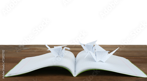 Origami cranes on notebook on wooden table, on white background