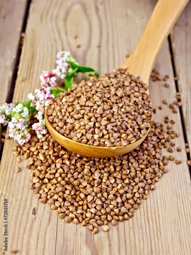 Buckwheat in wooden spoon with flower on board Buckwheat in wooden spoon with flower on board